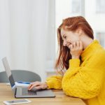 Young,Cheerful,Red-haired,Woman,In,Yellow,Sweater,Using,Laptop
